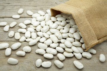 Large White Beans Poured Out of a Burlap Bag on a Wooden Table