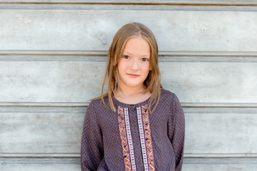 Close up portrait of a cute little girl of 8 years old against grey wooden background, wearing brown blouse