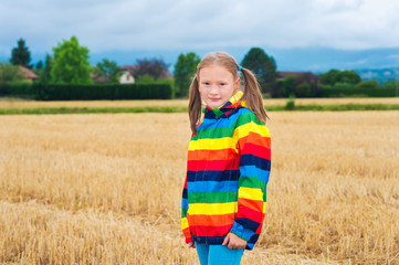Adorable little girl playing in a field, wearing rainbow rain coat