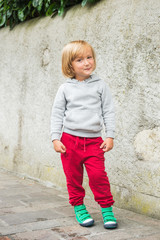 Fashion portrait of adorable toddler boy wearing grey sweatshirt, red trainings and green shoes