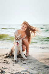 young caucasian female with siberian husky puppy playing on beach
