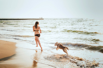 young caucasian female with siberian husky puppy playing on beach