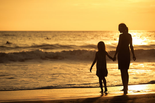 Mother and daughter playing on the beach at the sunset time.