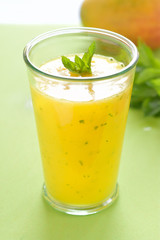 Cooling Mango mint smoothie, summer drink on green table, Yellow Tropical Smoothie made with mango, mint and lime juice.