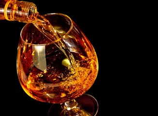 Fototapeta na wymiar barman pouring snifter of brandy in elegant typical cognac glass on black background