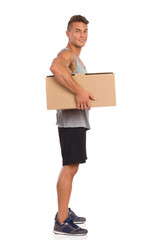 Muscular Man Holding Carton Box Under His Arm. Side view. Full length studio shot isolated on white.