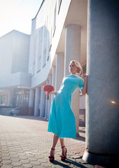 The girl in a blue dress with red flowers in a town near a large