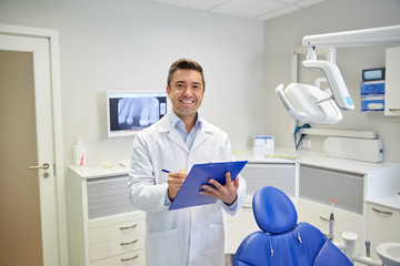 happy male dentist with clipboard at dental clinic