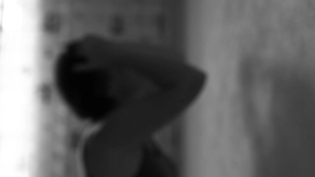 Woman standing at the wall and suffering. Defocused. Black and white.
