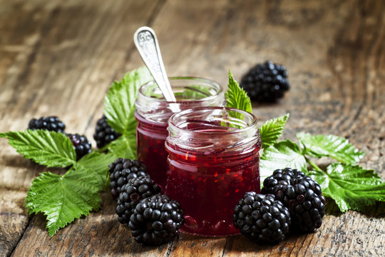 Two jars of blackberry jam, fresh berries and green leaves in an