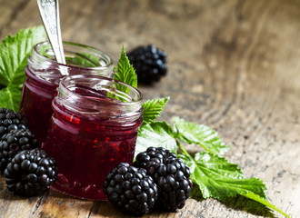Two jars of blackberry jam, fresh berries and green leaves in an