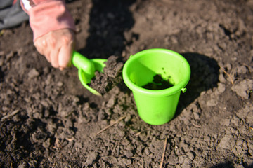 Girl playing in the mud with green toy bucket and spade