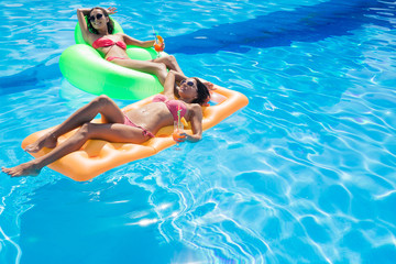 Girls holding cocktails and lying on air mattress