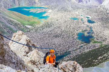Mountain climber over abyss Elder man orange jacket protection helmet holding belaying rope rocky...