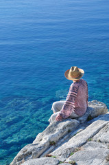 Woman sitting on the rock near the sea and enjoying the beautiful blue sea color 