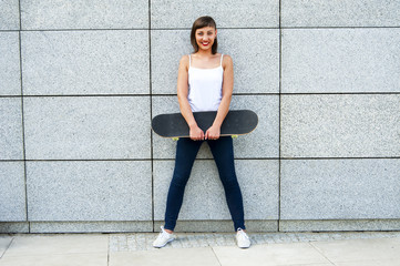 Plakat Young girl with skateboard in the city by the wall smiling.