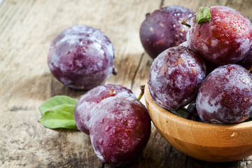 Large purple plum with water drops and leaves in a wooden bowl,