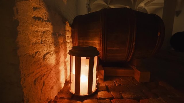 Detail of a barrel in an old cellar with a flickering light in the background
