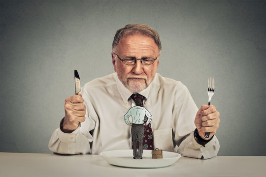 businessman with knife and fork looking at his employee on a plate