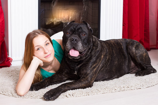 Girl lying near the fireplace with dog Cane Corso