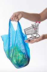 Woman holding tiny supermarket trolley and plastic shopping bag