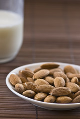 Whole almonds served on a small white plate with a glass of milk in the background