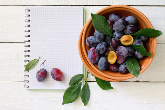 Plum in a ceramic bowl and a notebook on a white wooden table