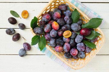 Plum in a wicker basket on a white wooden table, top view