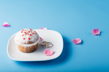 Colorful muffin on saucer with flower petal and wedding rings