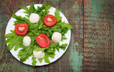 Green salad made with arugula, tomatoes, cheese mozzarella balls and sesame on plate