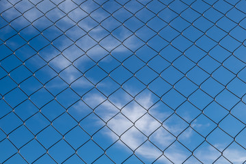 iron fence on a blue sky with small clouds
