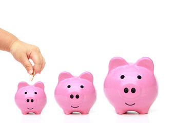 hand of a young baby giving golden coin to a piggy bank sitting on pile of golden coins