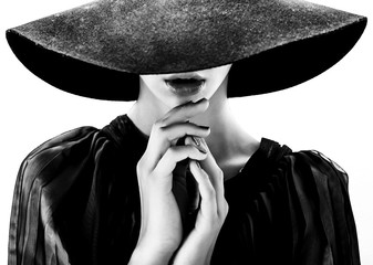 Beautiful woman with full lips in black hat poses on white - obrazy, fototapety, plakaty