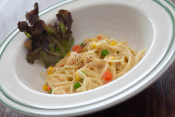 Dish of spaghetti carbonara with carrots, corn, peas, shrimp.