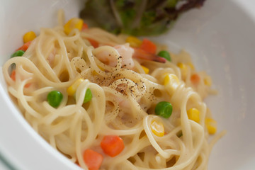 Dish of spaghetti carbonara with carrots, corn, peas, shrimp.