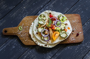 grilled chicken breast, fresh vegetables - tomatoes, cucumbers, zucchini, onions, peppers and homemade tortilla on a dark wooden background