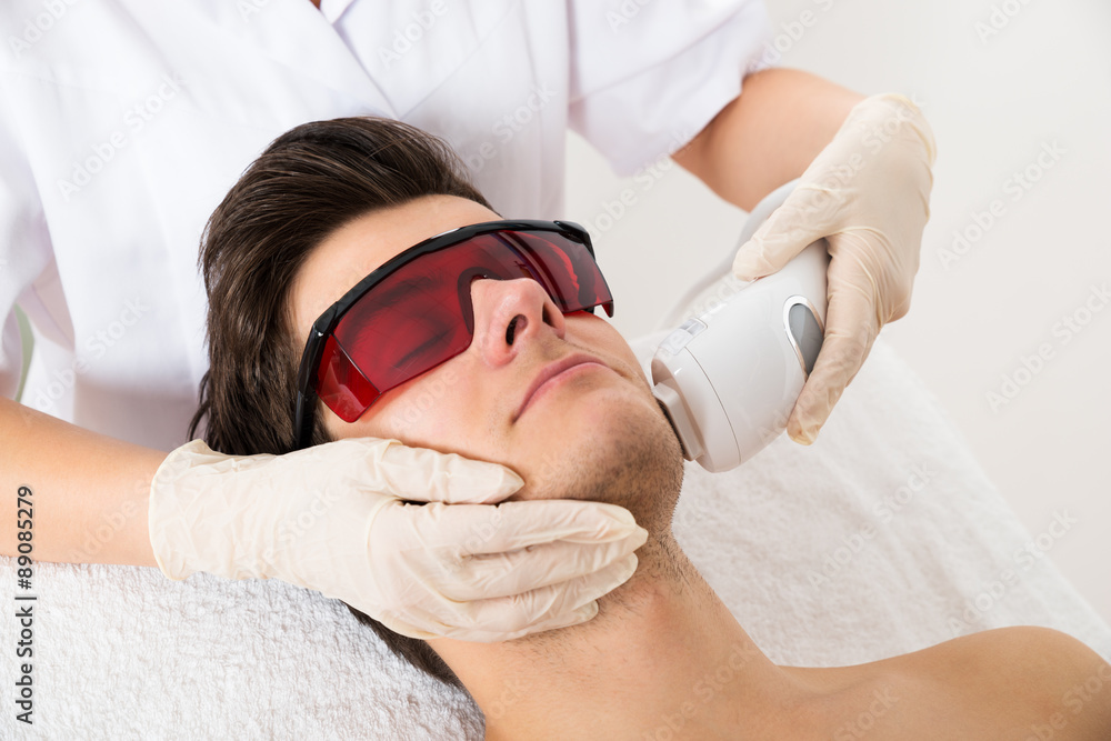 Wall mural beautician giving laser epilation treatment to man face