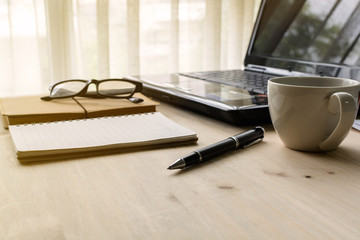 Cup of coffee with laptop on wooden desk and stack of document