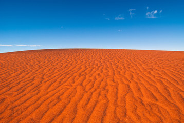 A rippled red sand dune against a clear blue sky, taken near Uluru in central Australia