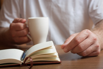 Male hand writing in a notebook and holding a cup of coffee