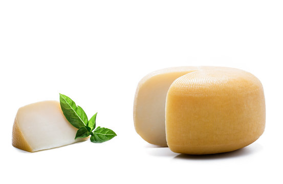 Yellow round cheese with a piece and basil leaves on white background