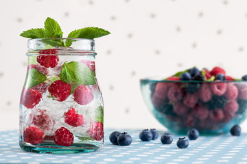 Fresh raspberry mojito and a glass bowl with berries on a white polka-dotted background