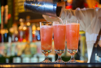 bartender spills cocktails from a shaker on glasses