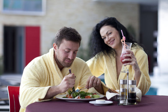 Cute couple in bathrobes having breakfast together at hotel