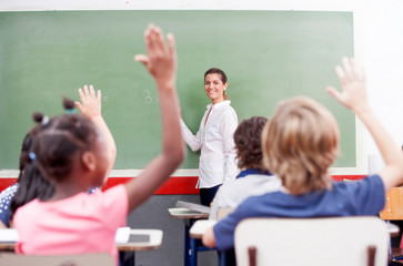 Happy schoolchildren at primary school raising hand in elementar