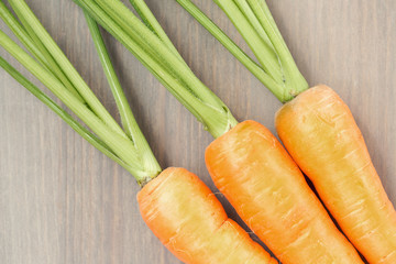 Raw carrots with green tops on wooden background