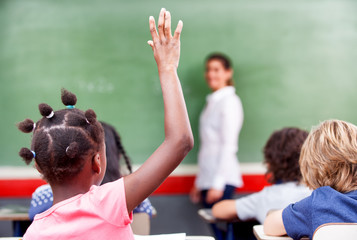 Happy schoolchildren at primary school raising hand in elementar