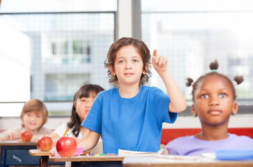 Portrait of cute boy raising hand at workplace with his classmat