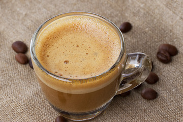 Cappuccino with crema in transparent cup on sacking.with coffee beans close