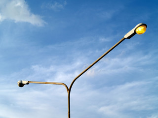 steel street light post against cloudy blue sky, one light bulb is turn on